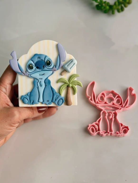 Cortador rosa impresso em 3D ao lado do topo de bolo azul que ele fez, com coqueiro e picolé
